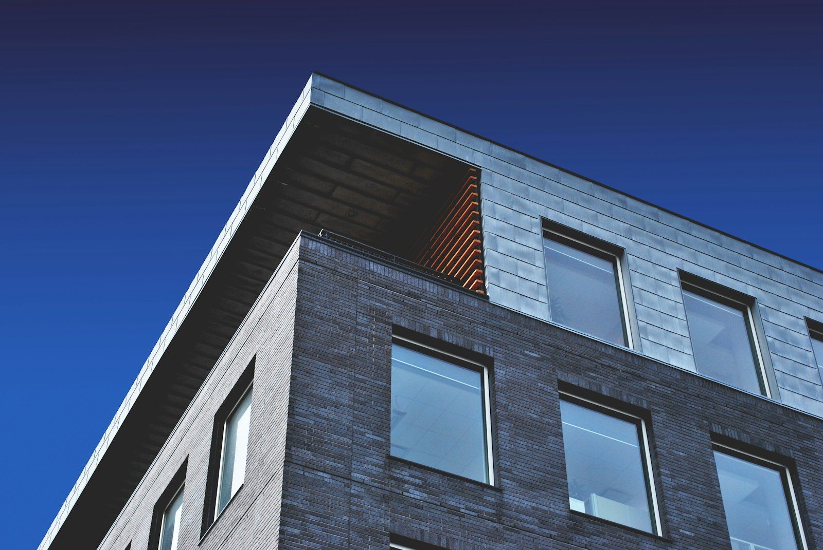 A Bansal Group mixed-use building corner — brick, zinc cladding, deep evening sky.